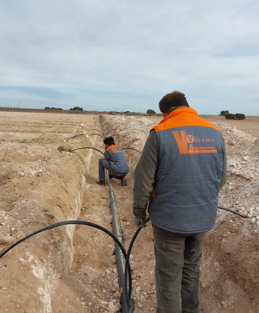 Equipo de Vicama Ingenieros instalando una tubería de riego en una zanja, en una parcela agrícola de Albacete