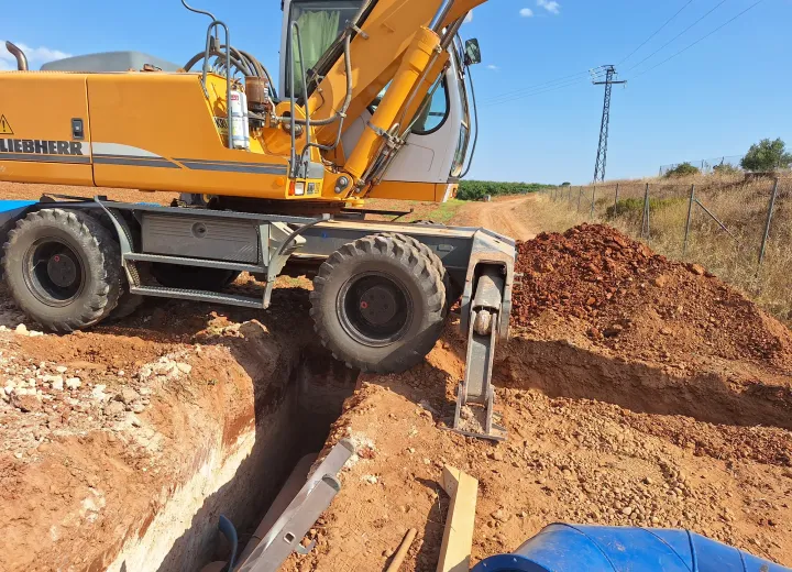 Retroexcavadora abriendo zanja para una conducción en una finca de Albacete, con línea eléctrica al fondo