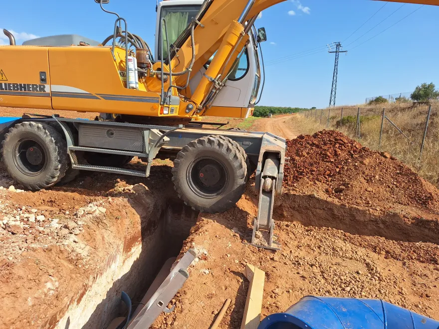 Retroexcavadora Liebherr abriendo zanja para una conducción en una finca agrícola, con línea eléctrica al fondo