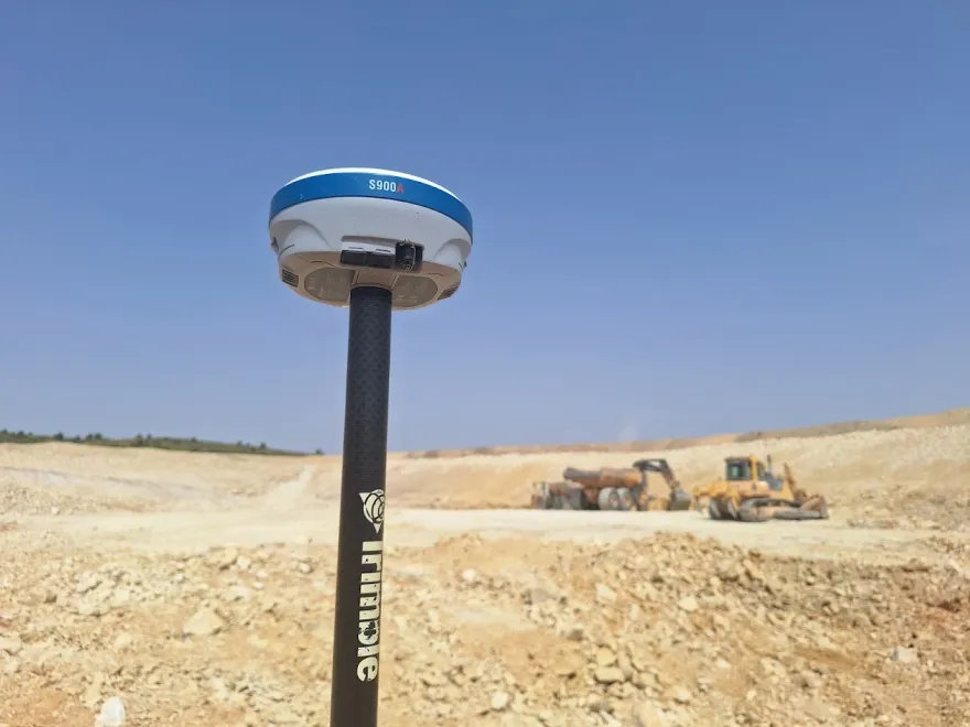 Receptor GNSS Trimble sobre jalón de fibra de carbono replanteando un movimiento de tierras, con bulldozer y camión cargado al fondo